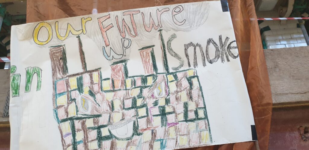 A large A2 banner features a child's drawing of a factory with fumes belching from chimneys. The text reads 'Our Future up in Smoke'